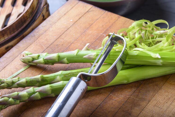 A vegetable peeler removes the woody stems at the base of asparagus