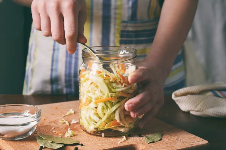 Woman cook sauerkraut or salad on wooden background. Step 5 - Put the cabbage in the jars. Fermented preserved vegetables food concept.