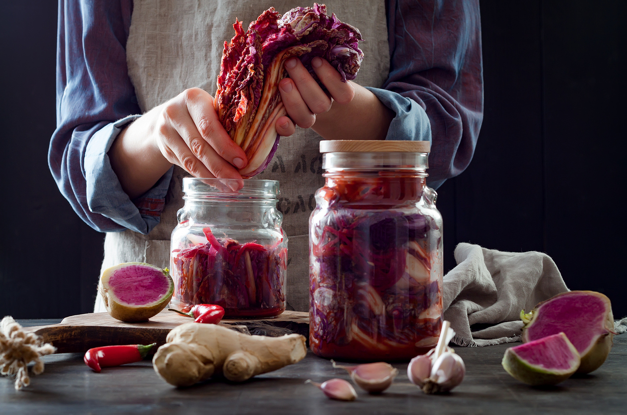 Cabbage kimchi in glass jar. Woman preparing purple cabbage and watermelon radish kimchi. Fermented and vegetarian probiotic food for gut health