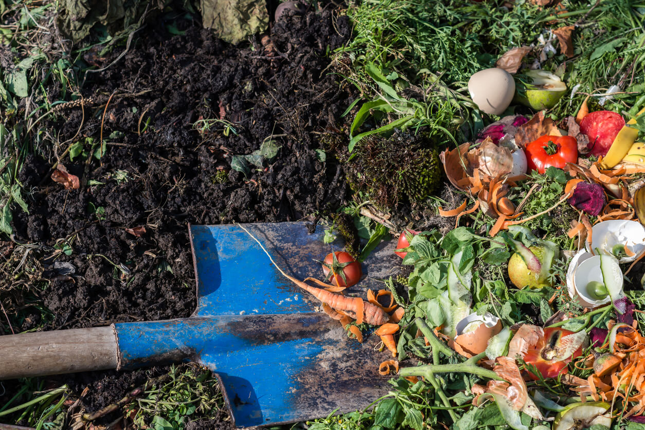 Compost box outdoors full with garden browns and greens and food wastes, blue shovel in the soil