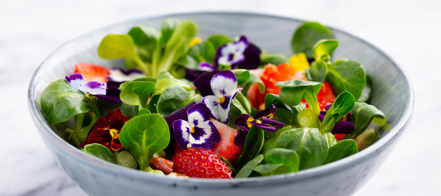 Fresh green salad with strawberries and edible flowers in a bowl