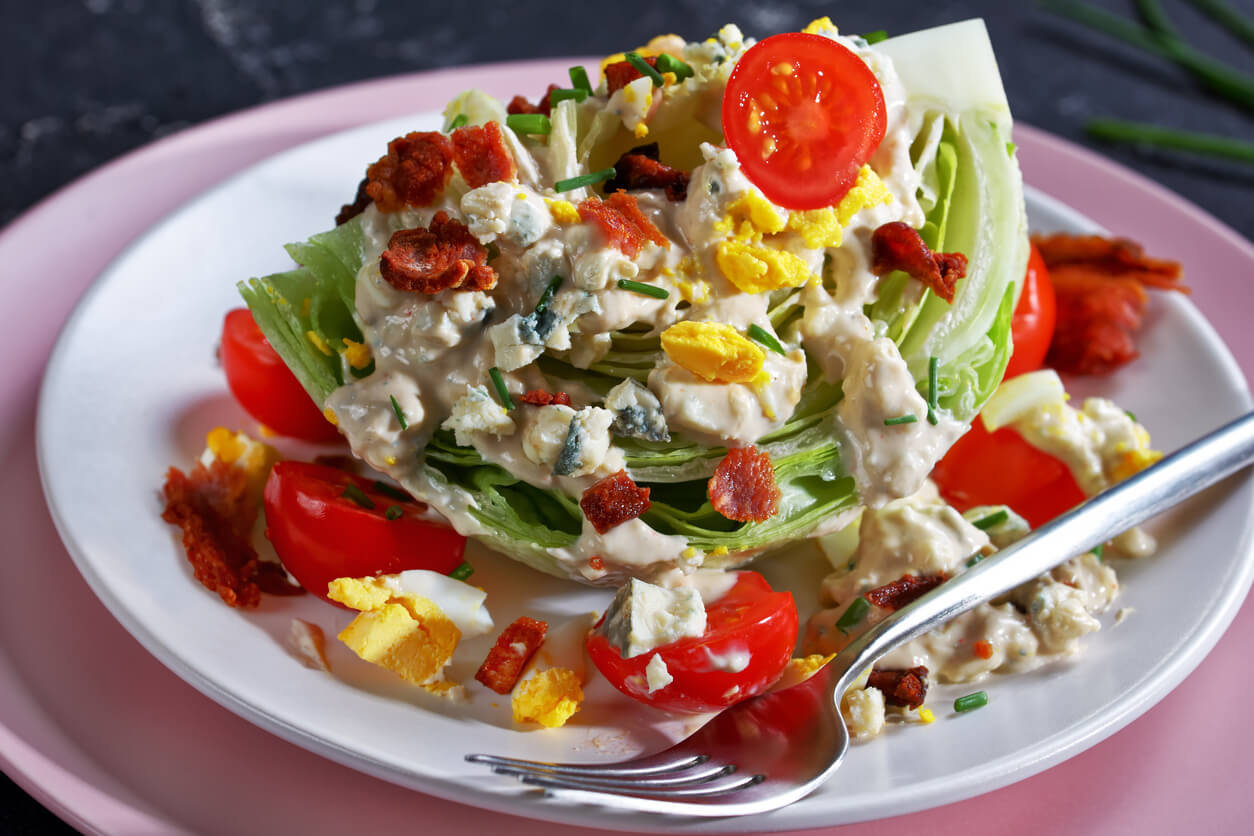 f iceberg wedge salad topped with blue cheese dressing, crispy fried bacon, cherry tomatoes, crumbled hard-boiled eggs