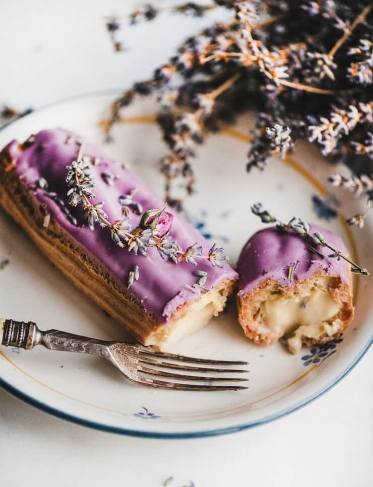 Lavender eclair with cream decorated with flowers and vintage fork
