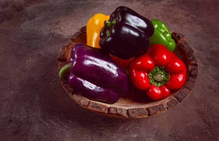 A collection of colorful bell peppers, in a wooden bowl, on a dark surface, top view, no people